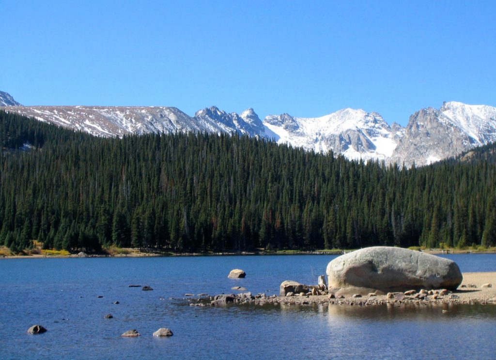 View of the snowcapped Continental Divide in Colorado with lake and huge rock in foreground