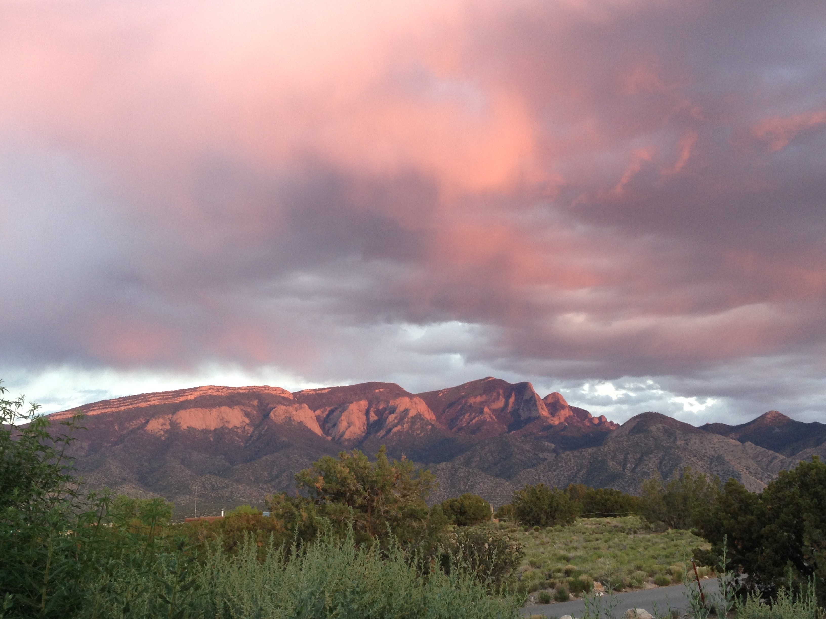 View of Sandia Mountains on a cloudy sunset, mountain face and clouds lit up bright pink.
