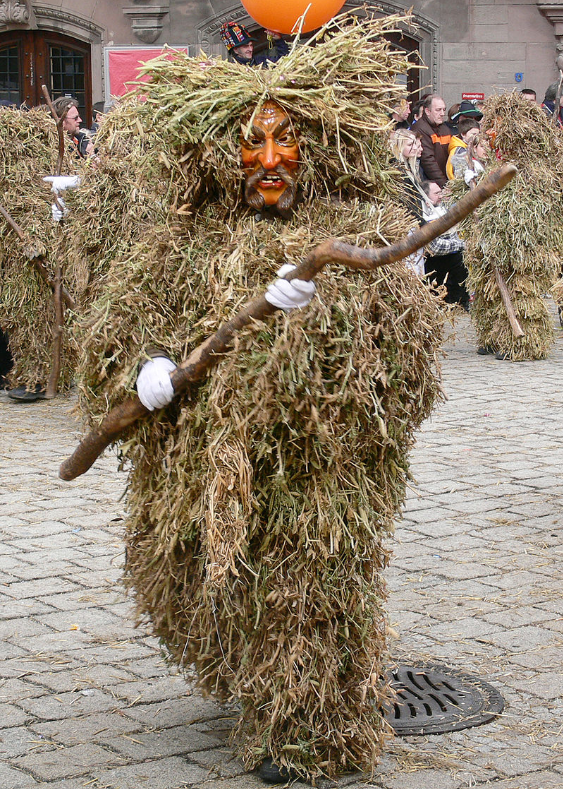Human in fuzzy straw costume with mask parading down a street