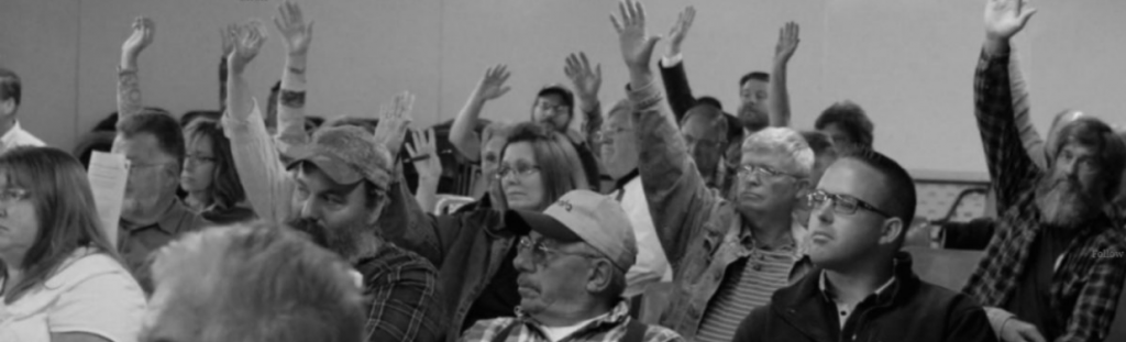 Regular folk in a public meeting raising their hands to vote for a community rights ordinance