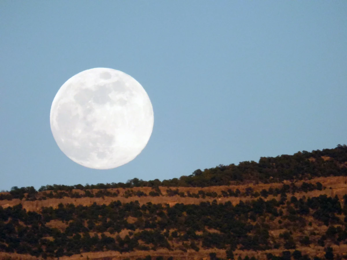 An enormous full moon just clearing a red rock cliff against a twilight sky.