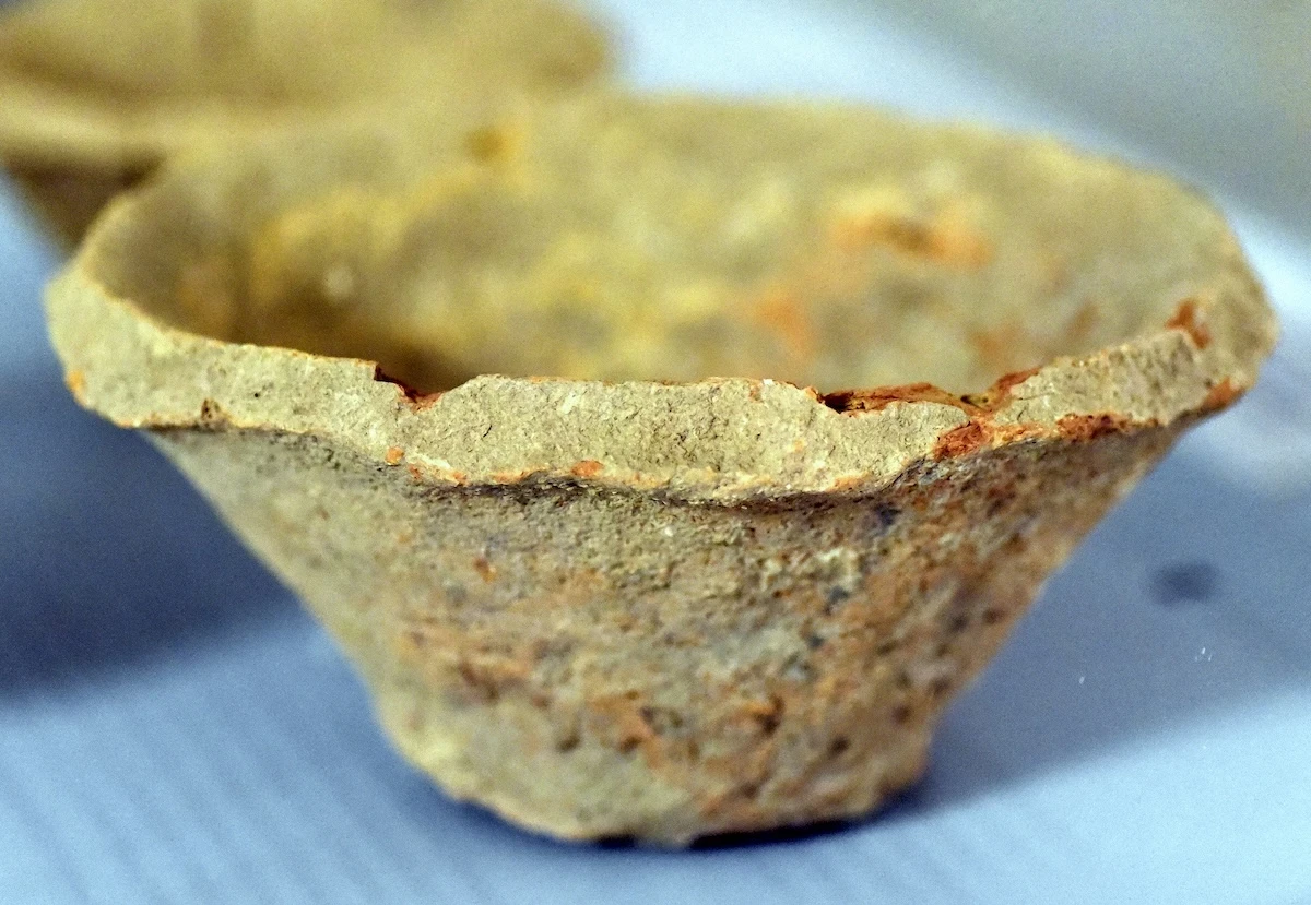A crude bowl with a narrow base and wider rim that is beveled at the top edge as if cut quickly with a knife. It’s really rough.