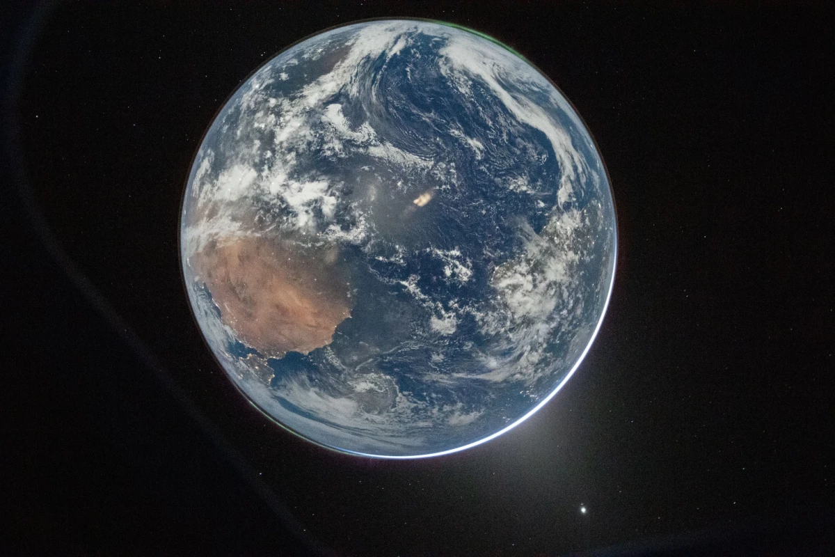 A view of Earth from the Orion spacecraft of the Artemis II mission to the moon. Australia is visible through clouds that swirl over land and oceans. A tiny rim of radiant sunlight outlines one edge of the world.