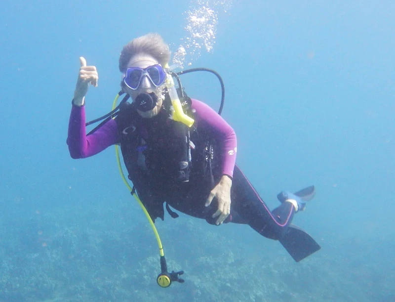 Scuba diver in black and lavender wet suit underwater waving. Cracks in personal life make new things possible, cracks of possibility.
