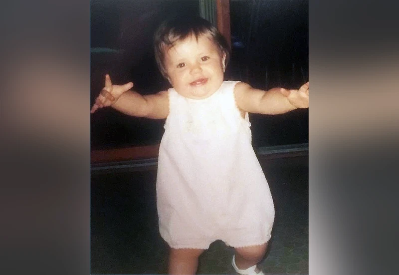 A toddler in a white onesie running toward you, arms outstretched, delight all over her face