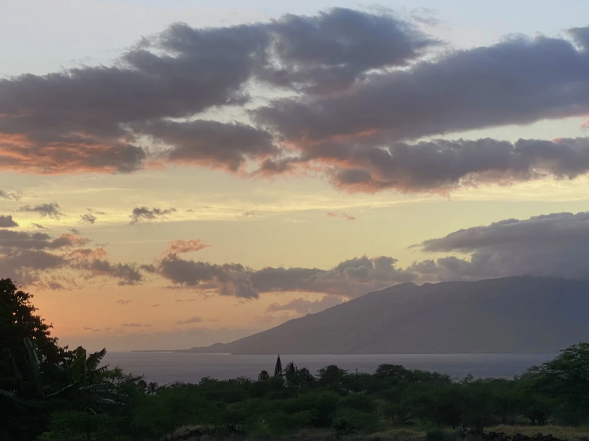 The same bay and mountain in sunset light, the sky tinged with orange, the gray clouds fired in red, and the water a dark blue-violet