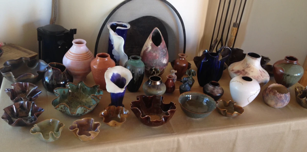 Dozens of ceramic pots of different shapes and colors and styles laid out on a table in front of a kiva fireplace