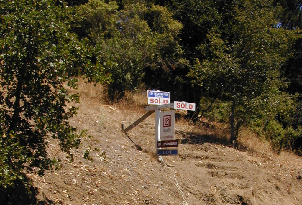 Realtor signs reading "Sold" pounded into a hillside lot under trees