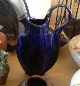 A cobalt-colored hand-built ceramic vase with tall curved handle