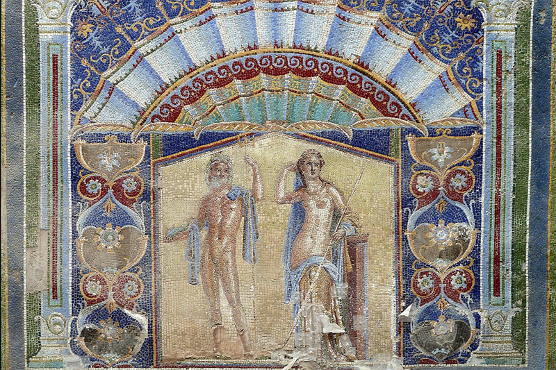 Photo alt text: Large formal mosaic showing an exceptionally beautiful man and woman—by Roman standards—naked but for elegantly draped shawls, surrounded by large stylized flowers and winecups and symmetric designs like waves of the sea in rich colors of gold and blue and burgundy.