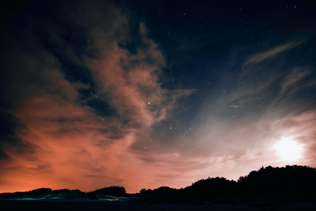 Pink lighted clouds at the horizon under a midnight blue sky twinkling with stars