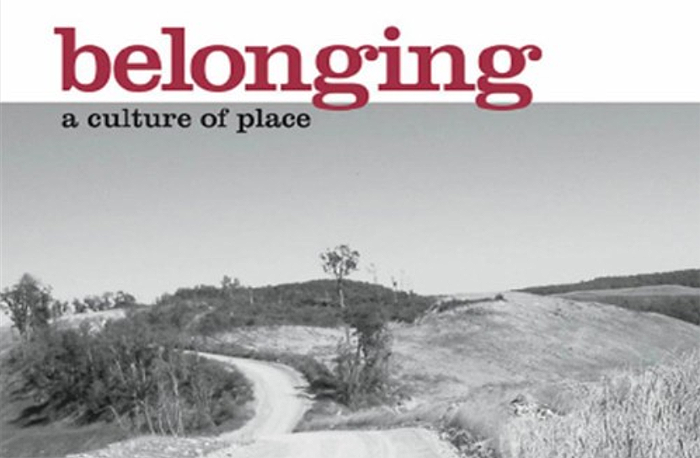 Detail from cover of bell hooks's book Belonging: A Culture of Place. A gray-scale photo of grassy hills under a wide sky, with a dirt road winding through