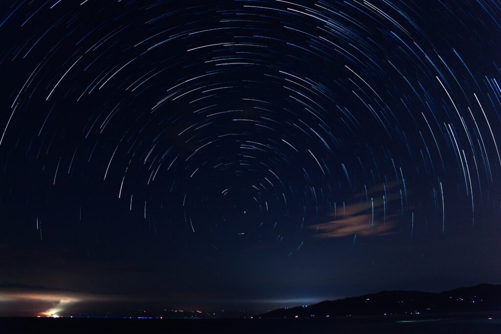 Night sky with star trails making a circle around Polaris near the horizon